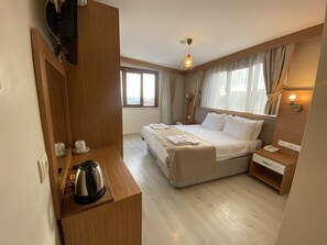 Ein Hotelzimmer mit einem Bett, einem Nachttisch, einem Wasserkocher, einem Spiegel, einem Fenster mit Vorhängen und einer Wandleuchte.