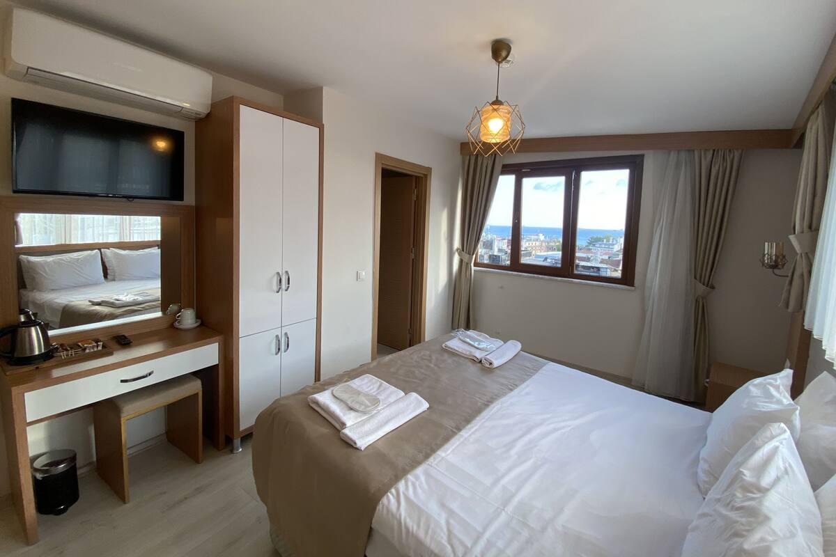 Et hotelværelse med seng, skrivebord med stol, fjernsyn, et vindue med udsigt og en loftslampe.