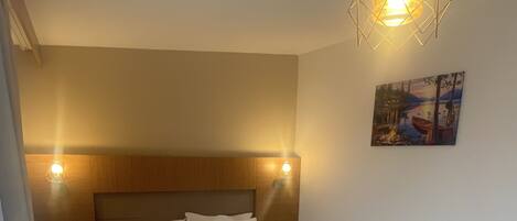 A neatly made bed with white linens and towels, a wooden headboard, and a painting on the wall.