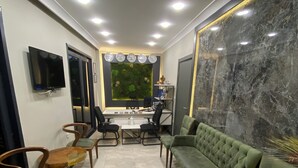Un salon moderne avec un canapé vert, des chaises en bois, une table basse, un téléviseur et une horloge murale.
