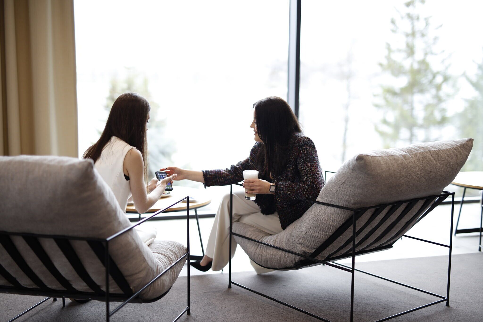 Deux personnes assises sur des chaises à rayures, face à face, avec une grande fenêtre en arrière-plan.