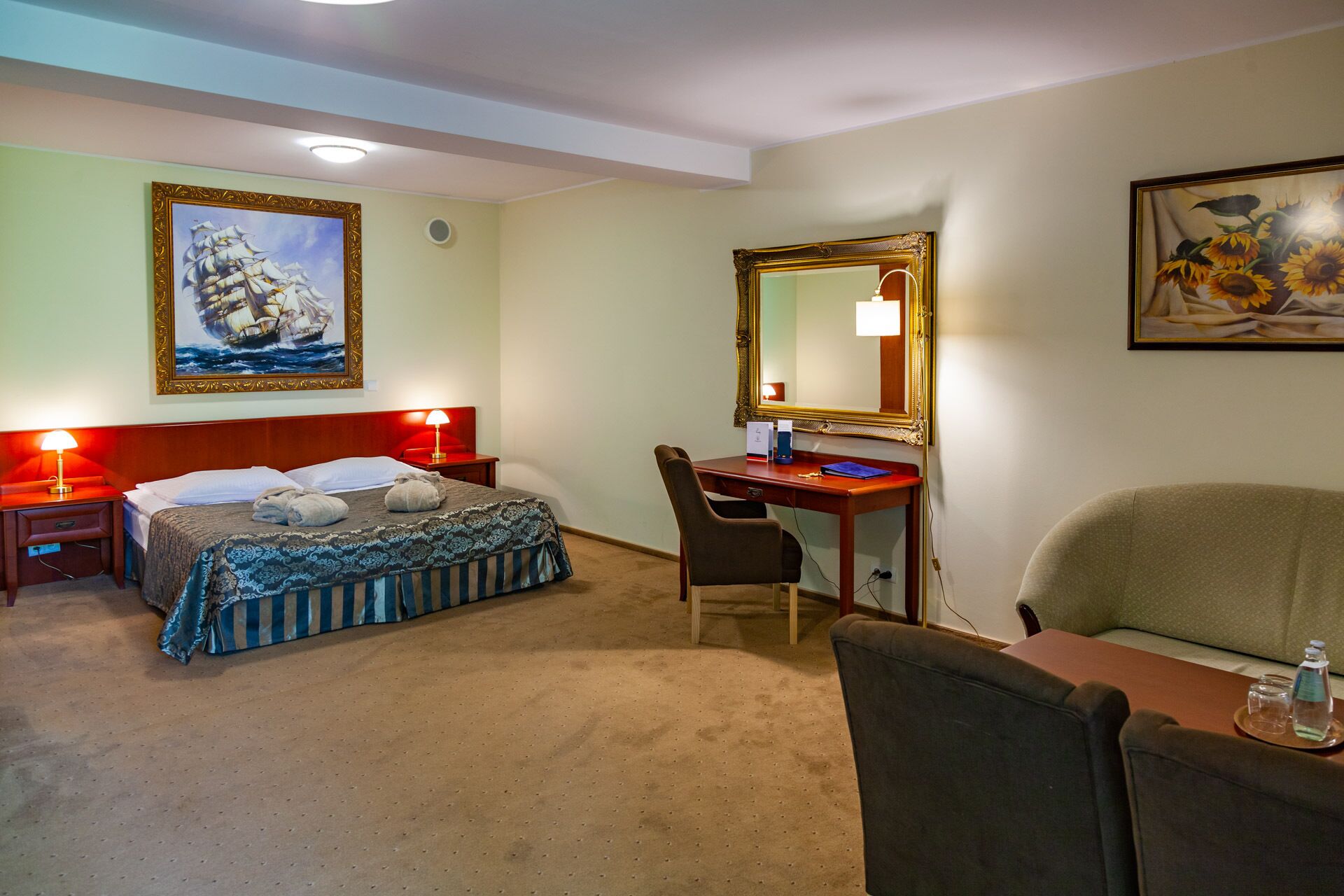 A hotel room with two beds, a desk, a chair, a large mirror, and artwork on the walls.