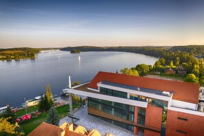 Un edificio moderno con techo rojo y amplios ventanales con vista a un lago tranquilo con veleros.