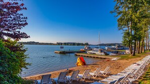 A lakeside beach with lounge chairs and a boat dock. - Hotel Robert's Port (Mikolajki)