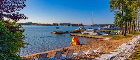A lakeside beach with lounge chairs and a boat dock.