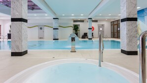 A large indoor swimming pool with marble columns, a hot tub, and a reception area with a desk and chairs. - Hotel Robert's Port (Mikolajki)