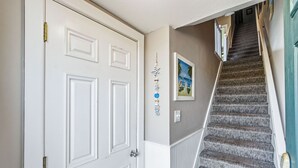 A staircase with carpeted steps leading to a landing, a white door with a brass handle, and a framed picture on the wall. - Fantastic Ocean Views, Community Pool, Dogs Welcome, Open Deck, KHSDA5 (Kitty Hawk)