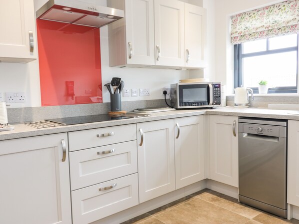 A modern kitchen with white cabinets, a red backsplash, a microwave, a dishwasher, and a window with a view.