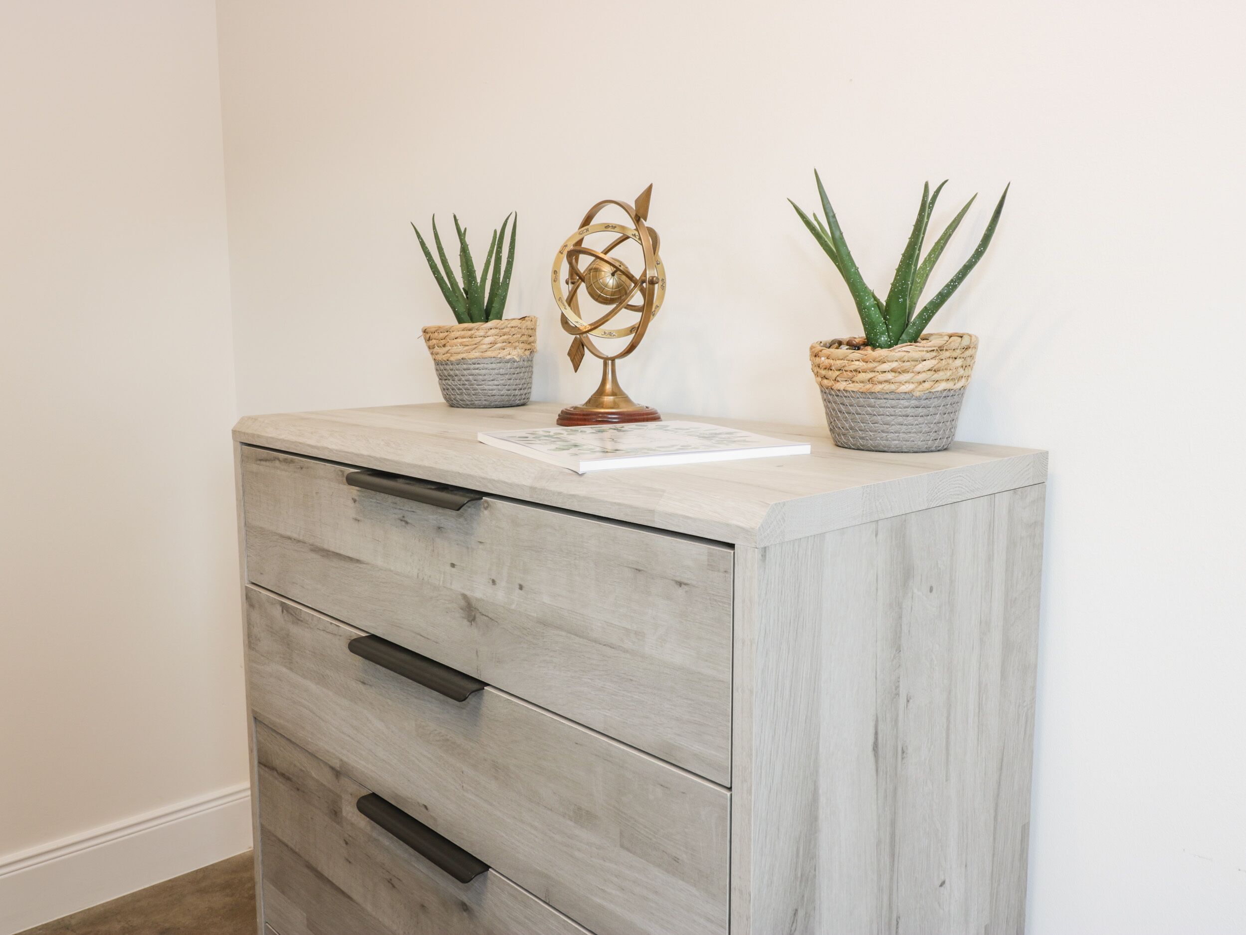 A wooden cabinet with two woven baskets containing green plants and a decorative metal piece.