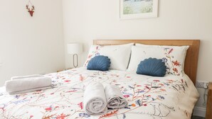 Una cama bien hecha con ropa de cama floral, dos almohadas y una toalla enrollada al lado.