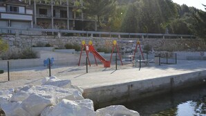 Un parque infantil junto al agua con toboganes y columpios, rodeado de un muro de piedra y una extensión acuática.