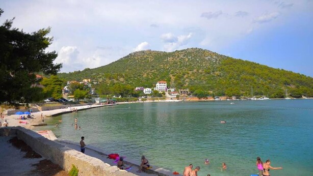 Una playa costera con agua cristalina, un muro de piedra y una colina al fondo.