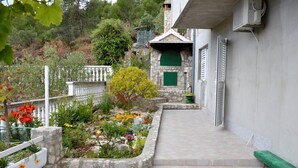 Un sendero estrecho que conduce a un edificio de piedra con una puerta verde, rodeado por un jardín con diversas plantas y flores.