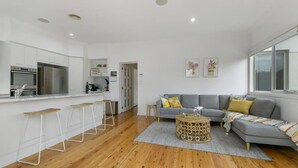A modern kitchen with white cabinets, a stainless steel refrigerator, and a bar area with stools. - Leafy Lamrock • Across from Park • Walk to CBD (Orange)