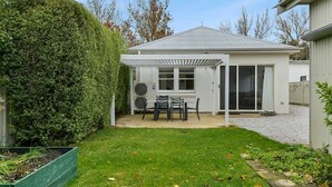 A small, single-story house with a covered patio, a lawn, and a tall hedge. - Leafy Lamrock • Across from Park • Walk to CBD (Orange)