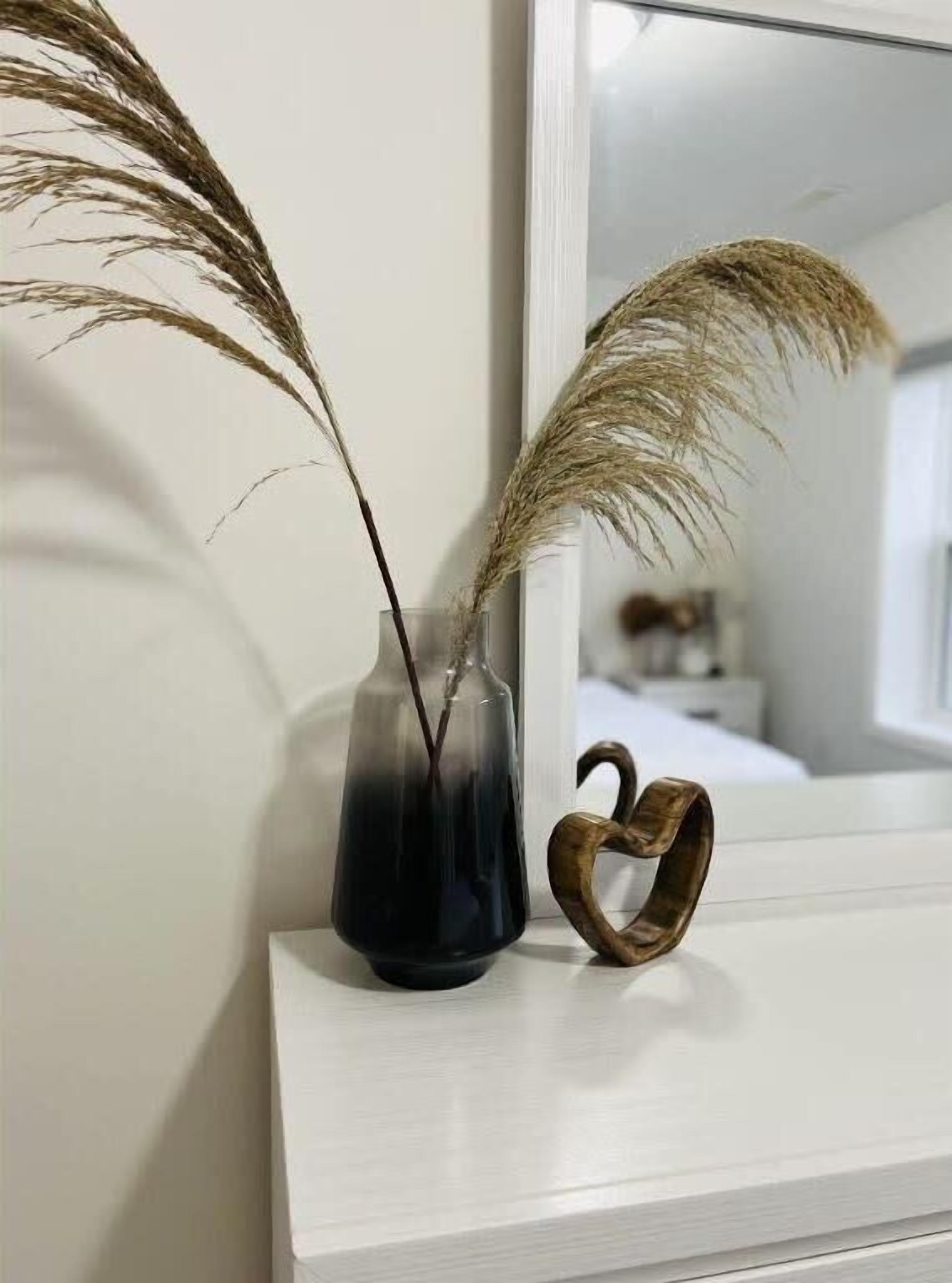 A vase with dried plants on a white shelf next to a mirror.