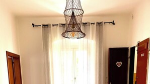 A room with a wooden floor, a sofa, a door with a heart-shaped decoration, and a hanging light fixture. - Giorgio's Dream (Chiavari)