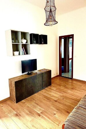 Una sala de estar moderna con suelo de madera, televisor de pantalla plana, aparador de madera oscura y lámpara colgante.