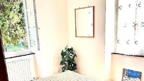 A bedroom with a bed, a window, a radiator, a plant, and a framed picture on the wall. - Giorgio's Dream (Chiavari)