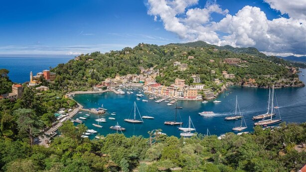 A coastal town with a marina filled with boats, surrounded by lush greenery and buildings with Mediterranean architecture. - Giorgio's Dream (Chiavari)