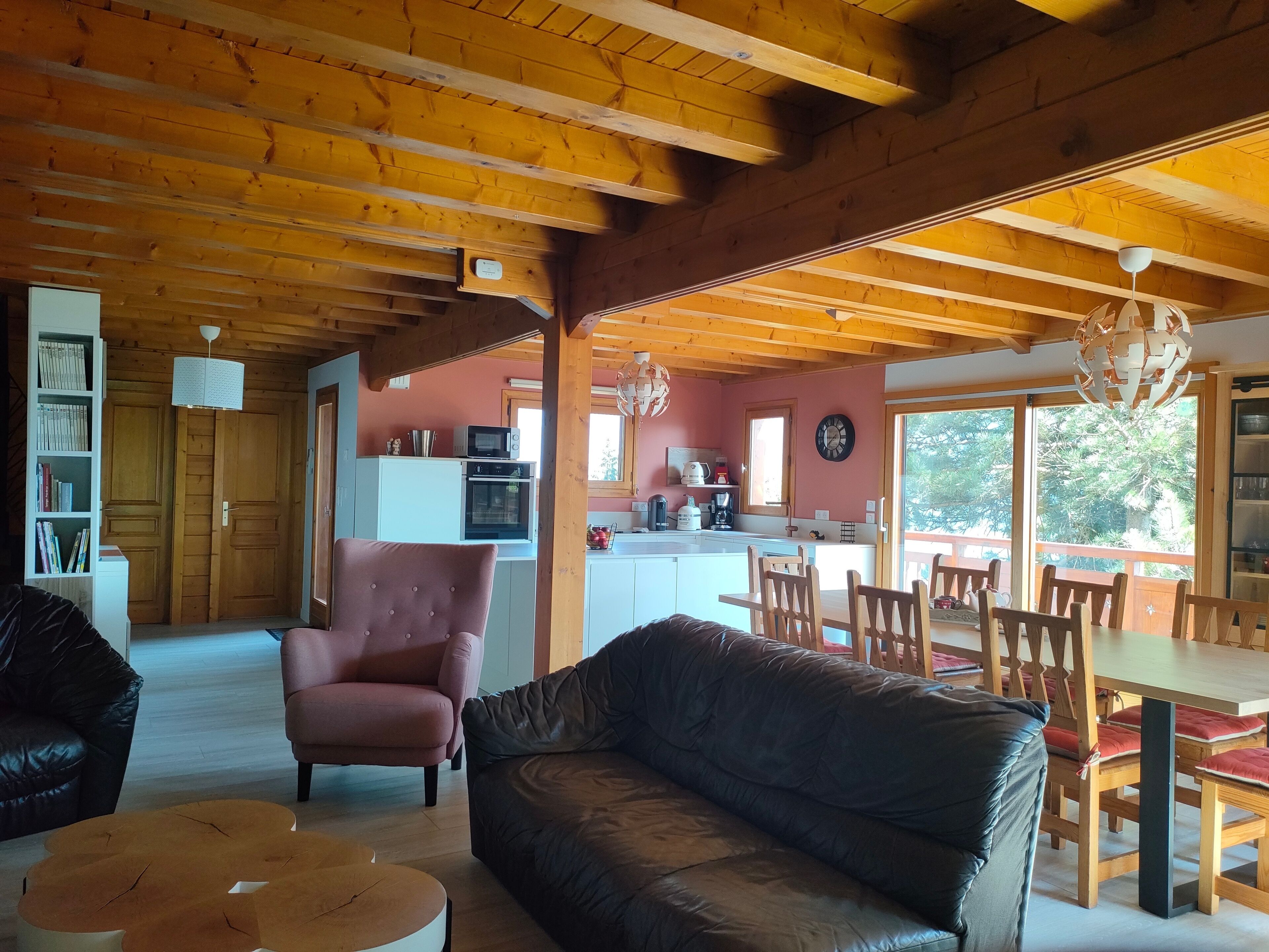 A cozy living room with a leather sofa, a coffee table, and a wooden dining table with chairs. There's a kitchen area with a microwave and a coffee maker.