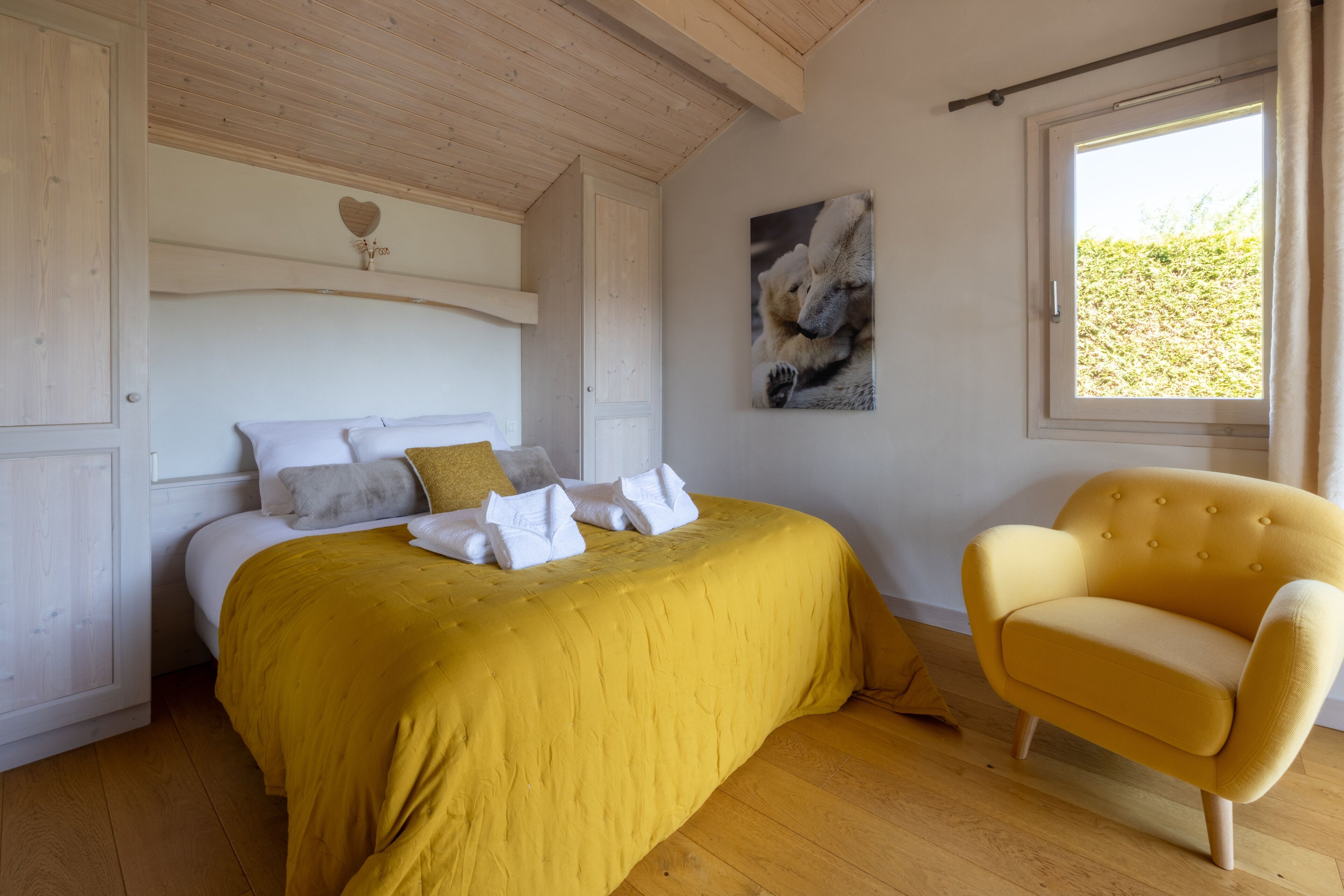 Une chambre à coucher avec un lit, un fauteuil jaune, une fenêtre et un tableau accroché au mur.