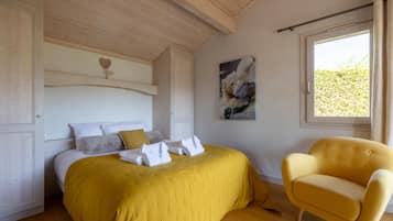 Une chambre à coucher avec un lit, un fauteuil jaune, une fenêtre et un tableau accroché au mur.