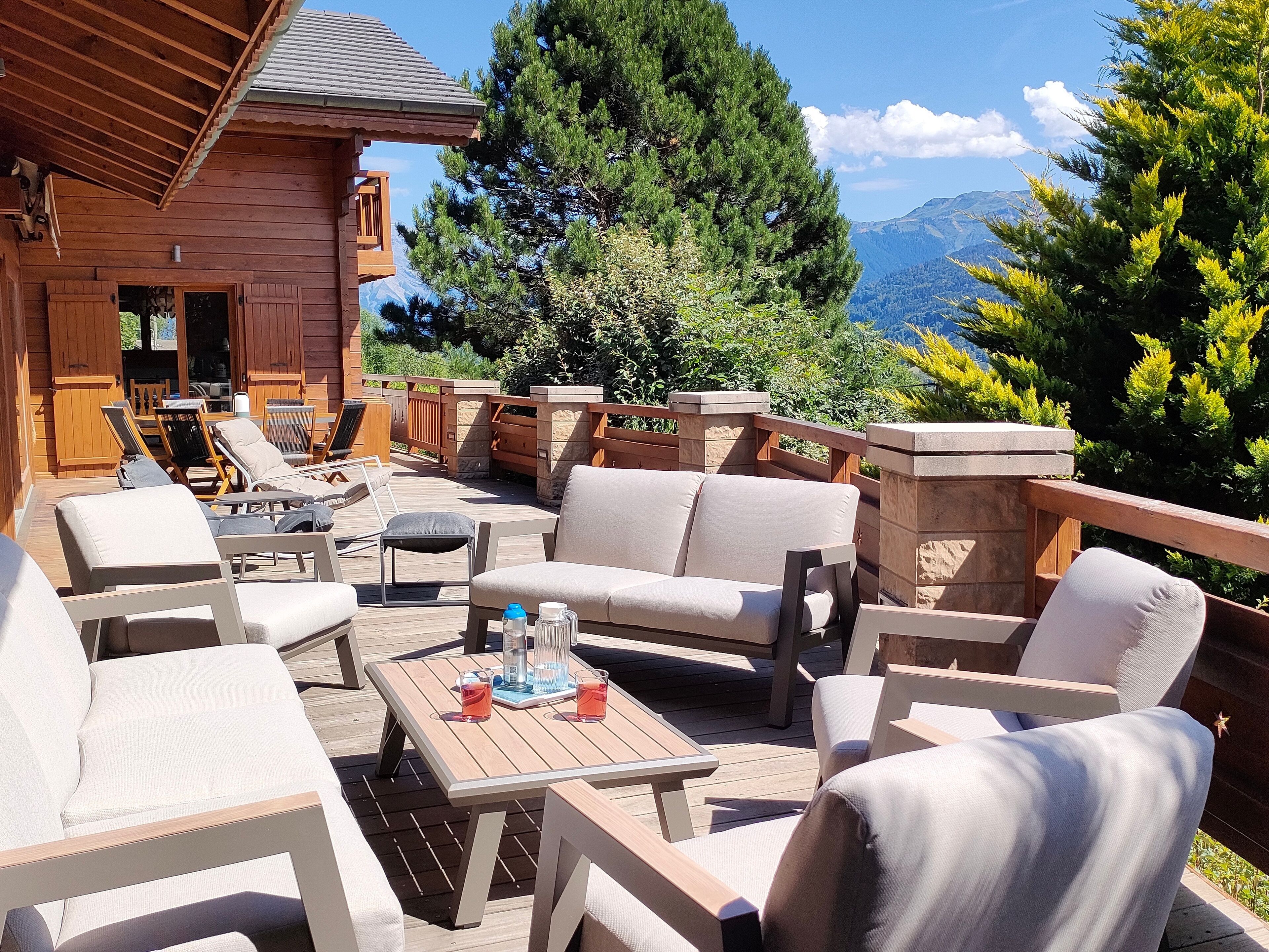 Une terrasse en bois aménagée avec du mobilier d’extérieur, notamment des canapés et des fauteuils, ainsi qu’une table avec des boissons.