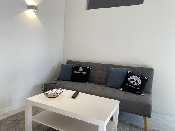 A modern living room with a grey sofa, two black cushions with white text, a white coffee table with a remote control, and a geometric wireframe lamp. - Apartment Schloofschdubb in Fuldatal bei Kassel (Fuldatal)