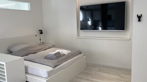 A modern bedroom with a bed, bedside lamp, and a mounted TV. - Apartment Schloofschdubb in Fuldatal bei Kassel (Fuldatal)