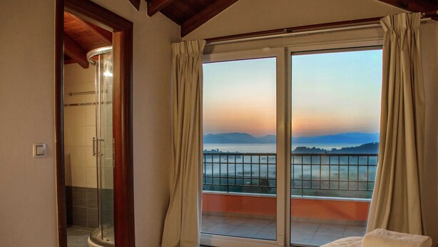 Une chambre dotée d’une grande porte-fenêtre coulissante donnant sur un balcon avec vue sur les montagnes et un plan d’eau.