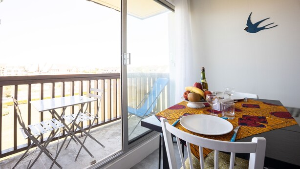 A balcony with a table set for dining, a chair, and a view of the city. - Sunan - Appartement avec balcon (Courseulles-sur-Mer)