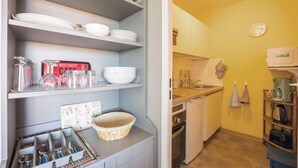A compact kitchen with shelves holding dishes and jars, a microwave, and a coffee maker. - Sunan - Appartement avec balcon (Courseulles-sur-Mer)