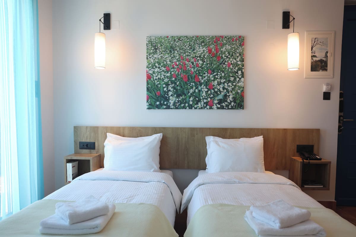 A hotel room with two beds, a large floral painting on the wall, and bedside lamps.