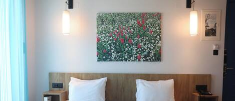 A hotel room with two beds, a large floral painting on the wall, and bedside lamps.