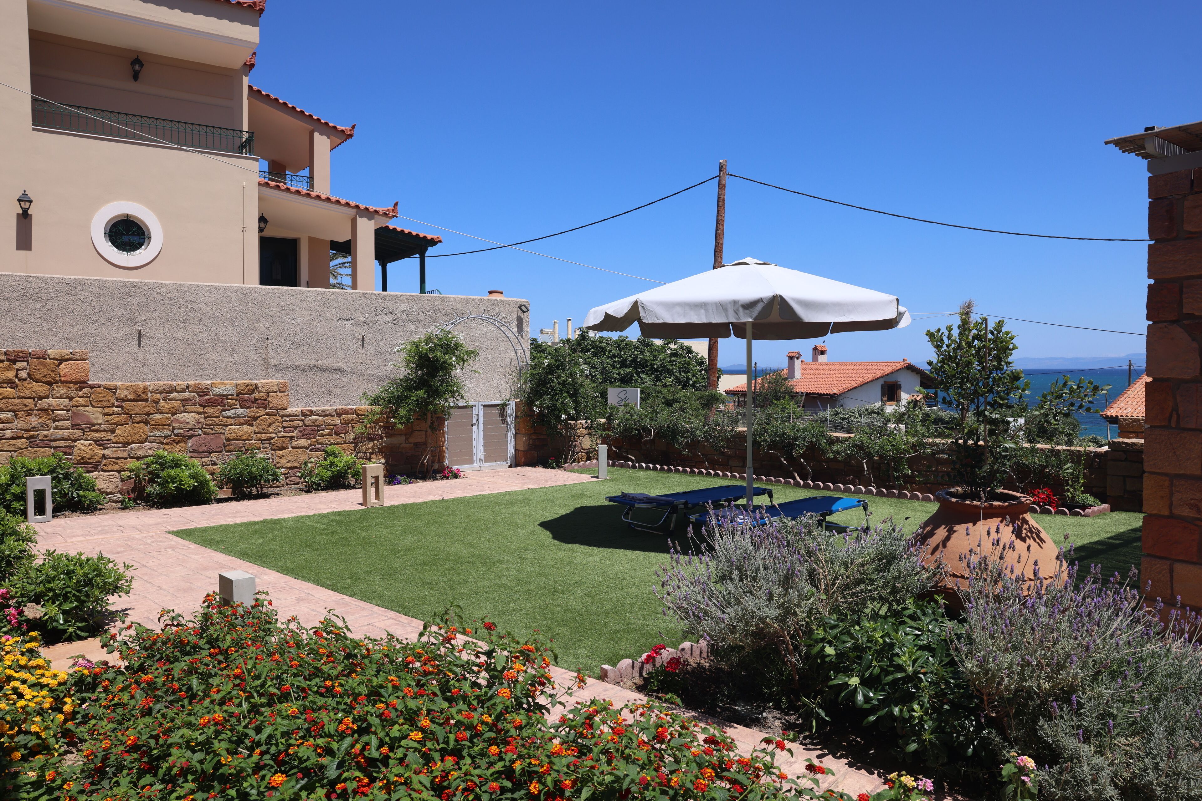 A well-maintained garden with a pool, a stone wall, and a view of the sea.