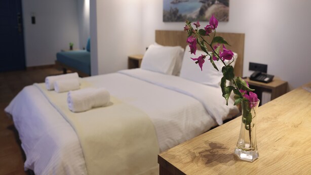 Een hotelkamer met twee bedden, een houten nachtkastje, een vaas met bloemen en een schilderij aan de muur.