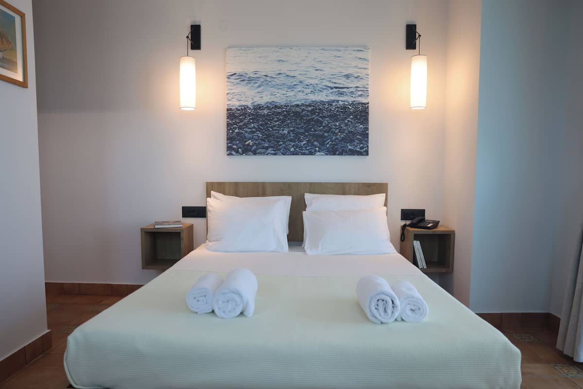 A hotel room with a large bed, two bedside tables, a painting of a beach scene, and wall-mounted lights.