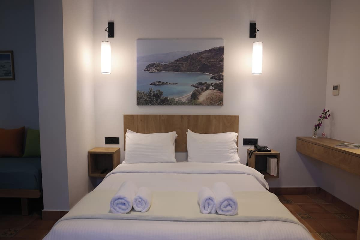 A hotel room with a bed, two bedside tables, a nightstand, a wooden bench, and a wall-mounted picture.