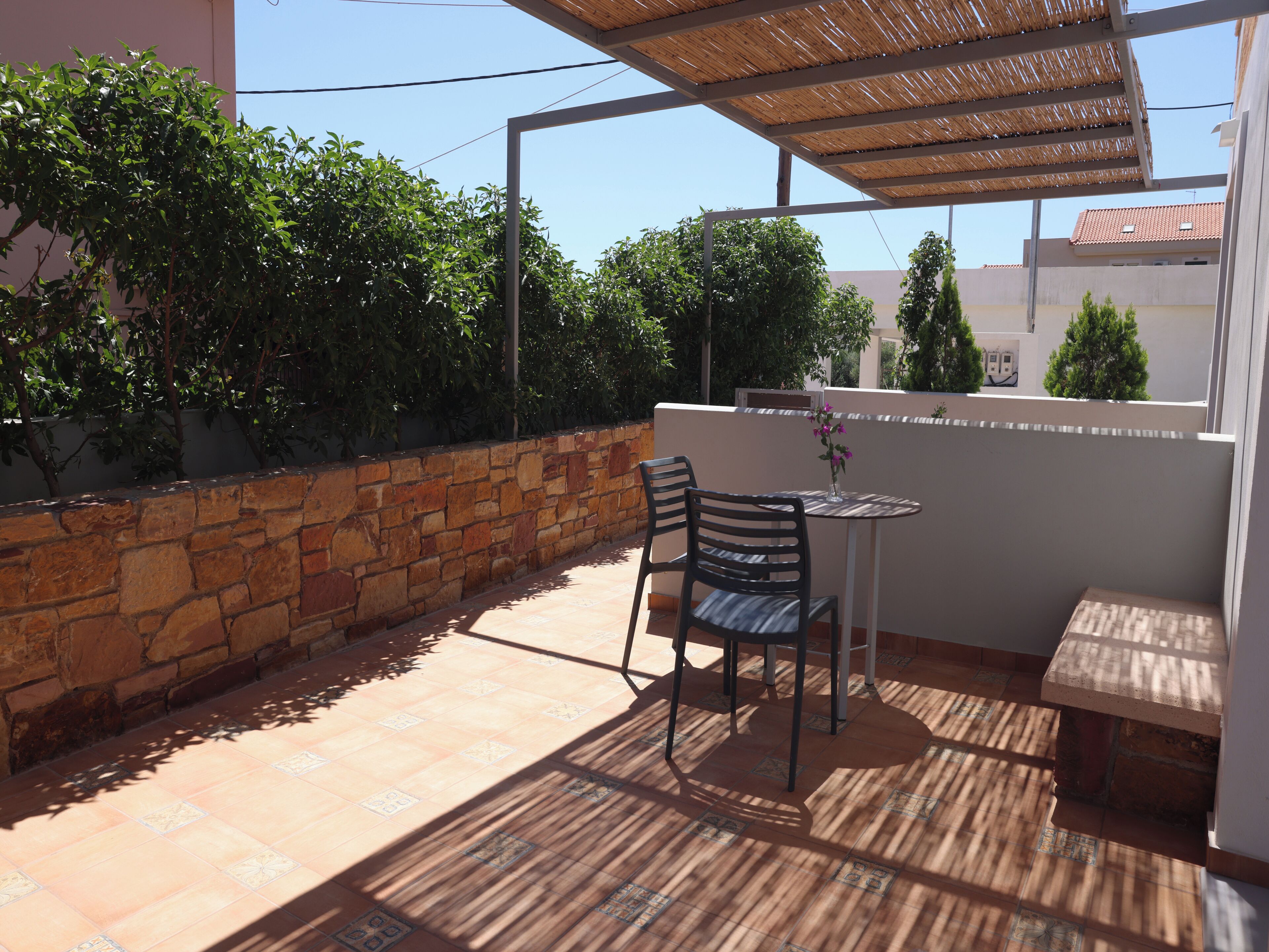 Un patio con mesa y sillas, un muro de piedra y una pérgola.