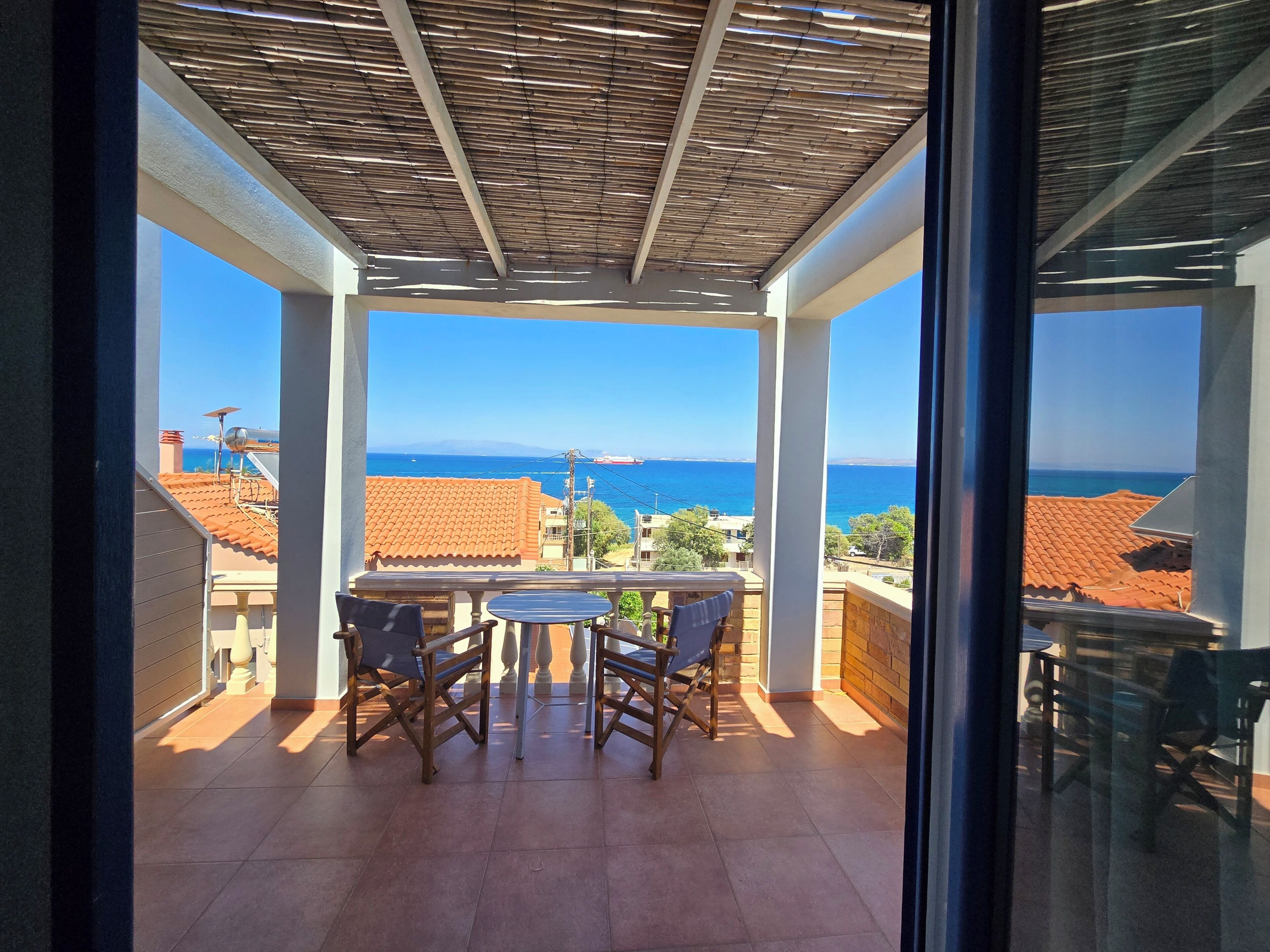A balcony with a view of the sea, a table, and chairs.