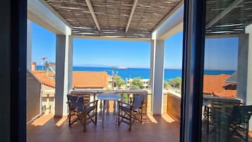 A balcony with a view of the sea, a table, and chairs.