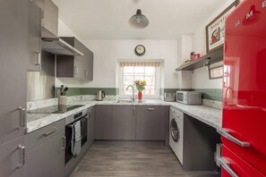 A compact kitchen with grey cabinets, a red refrigerator, a washing machine, and a clock on the wall. - Gorgeous Apartment with Rooftop Views, Central Bath (Bath)