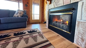 Un salon chaleureux avec une cheminée, des murs en bois, un canapé bleu et un tapis à motifs.