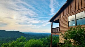 Une cabane en bois dotée d’un balcon donnant sur une vallée boisée.