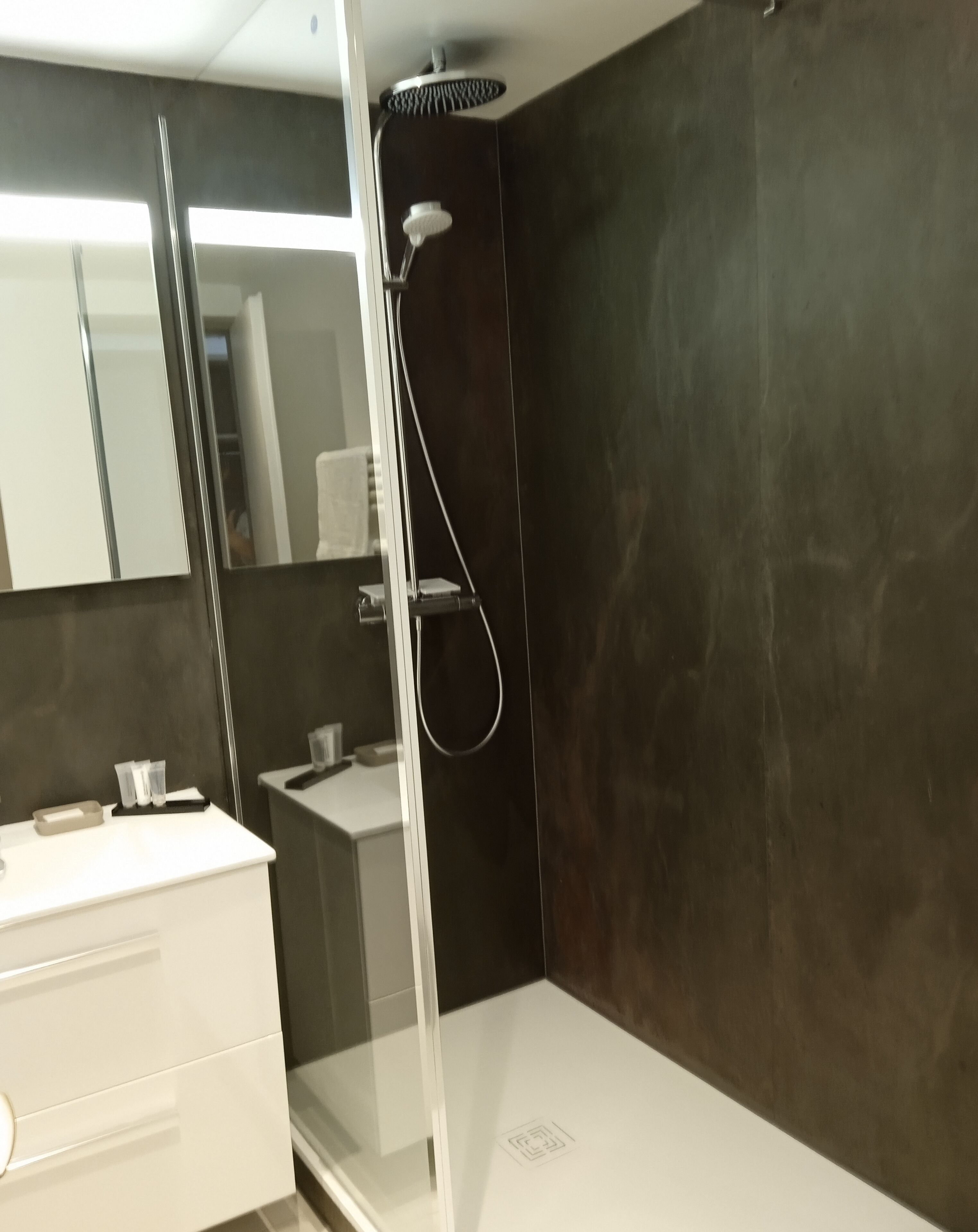 Un baño moderno con ducha, tocador con espejo y lavamanos blanco.