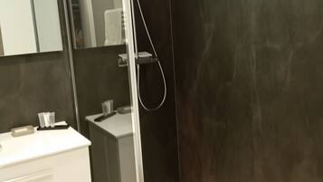 Un baño moderno con ducha, tocador con espejo y lavamanos blanco.