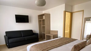 Une chambre à coucher avec un lit, un canapé noir, une télévision, une armoire et un bureau.