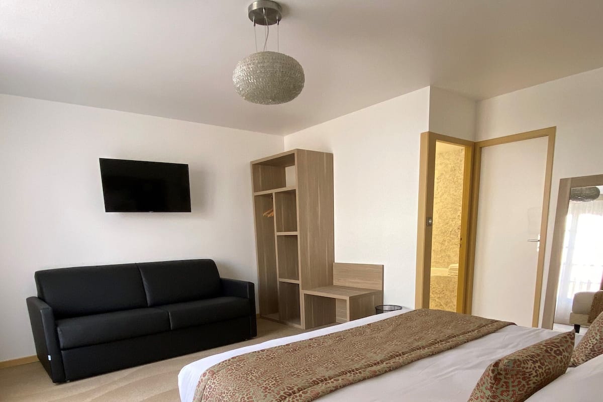 A bedroom with a bed, a black sofa, a TV, a wardrobe, and a desk.