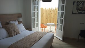 Une chambre avec un grand lit, une tête de lit en bois et une vue sur un espace extérieur aménagé avec une table et des chaises.